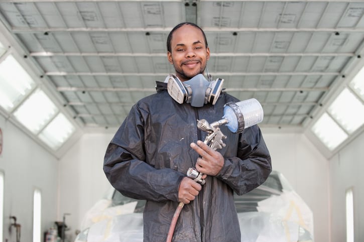 Carolina Collision and Frame Service | Paint technician holding a spray gun and smiling in front of a painted car