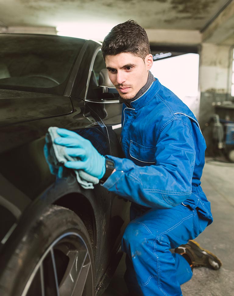 Carolina Collision and Frame Service | Mechanic wearing a blue jumper and gloves buffing out the paint on the side of a black car