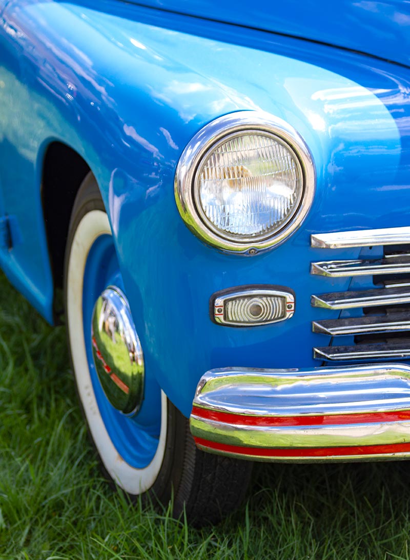Carolina Collision and Frame Service | close up view of a vintage blue car's headlight, chrome grill, and tire