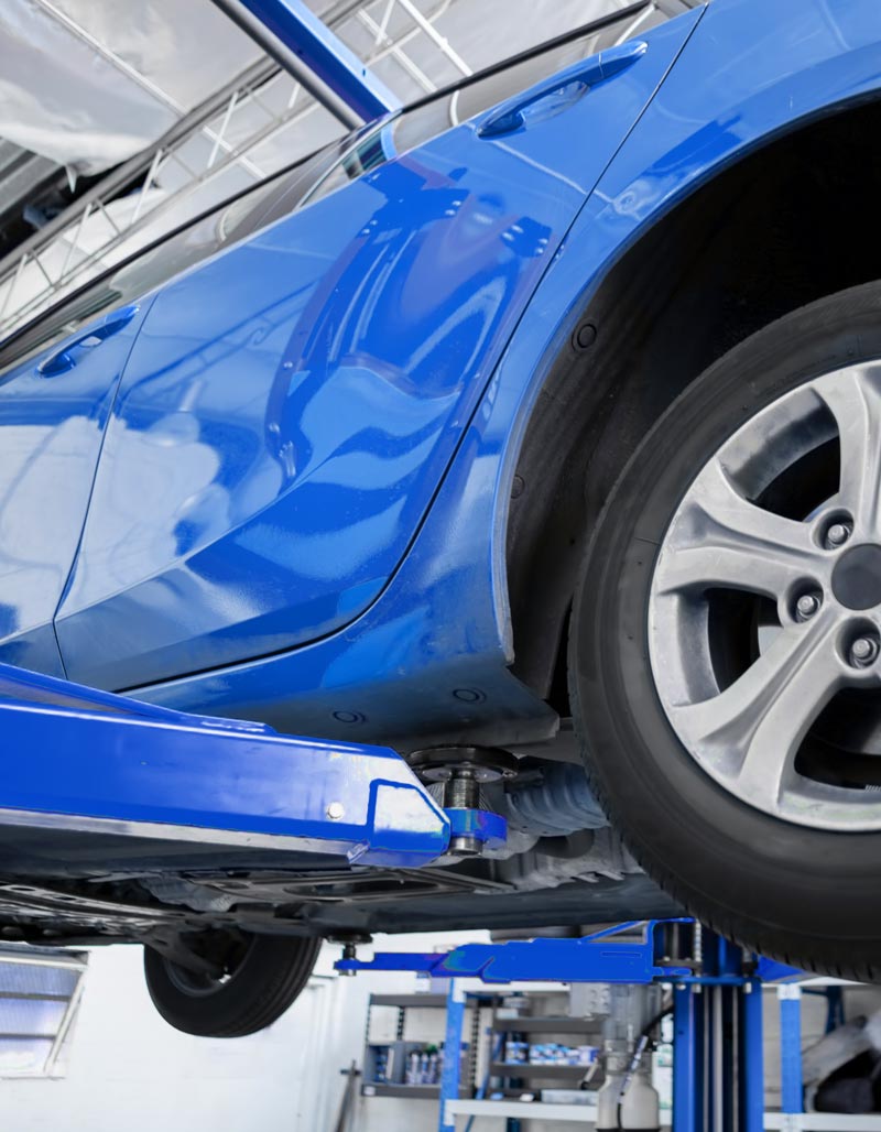 Carolina Collision and Frame Service | Close up view of a blue car on a blue lift in an auto repair shop